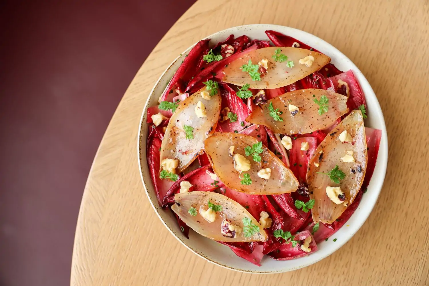 Credit Saffy_s.jpeg A bowl of roasted endives with walnuts and herbs resting on a wooden table at Saffy’s, one of the best Middle Eastern restaurants in Los Angeles you can book at OpenTable.