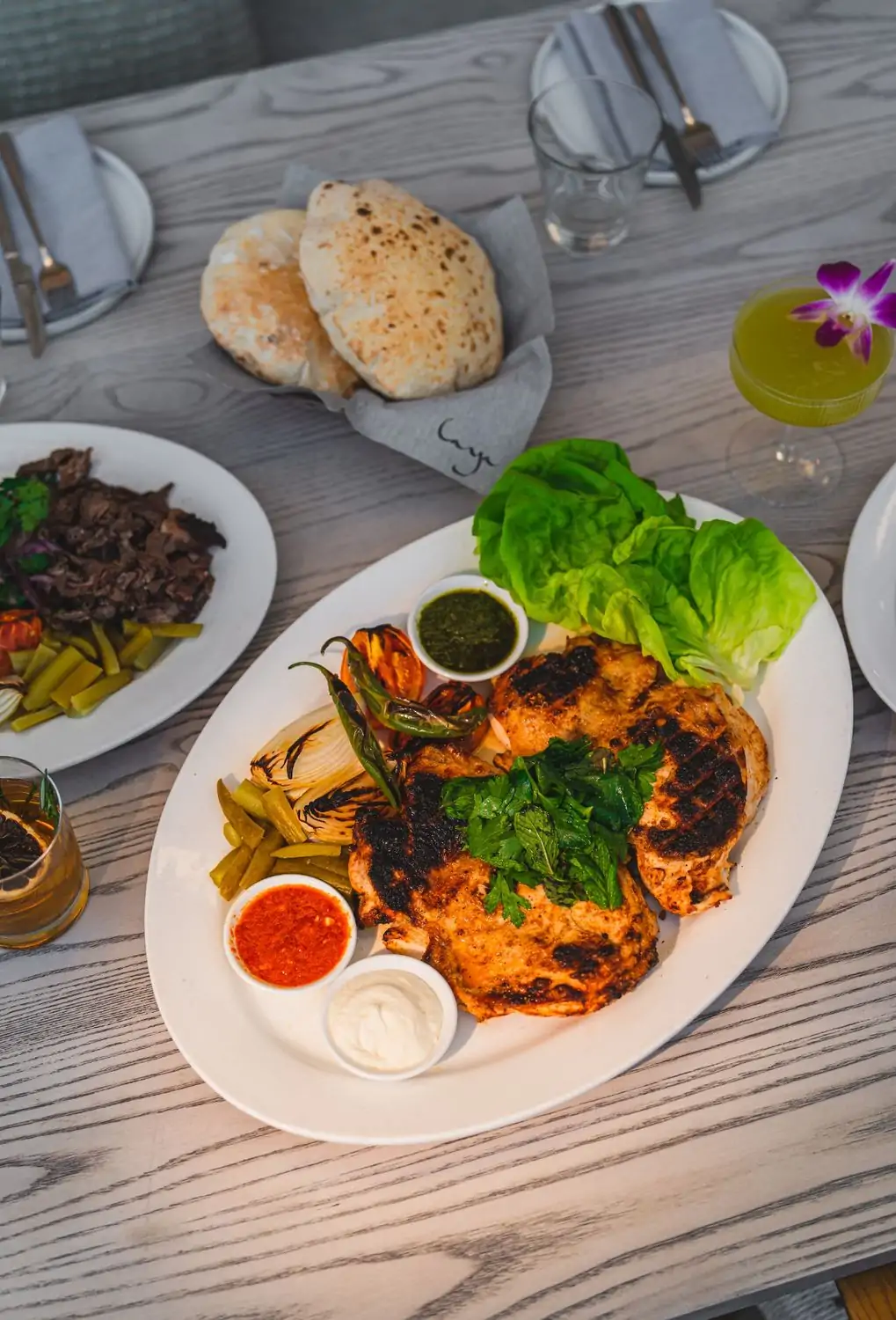 Credit Laya Restaurant.jpg A light wood table with a variety of Middle Eastern dishes, including grilled chicken, pita bread, salads, and dips. There are also cocktails and a glass of water on the table at Laya Restaurant in Hollywood, now available to reserve on OpenTable.