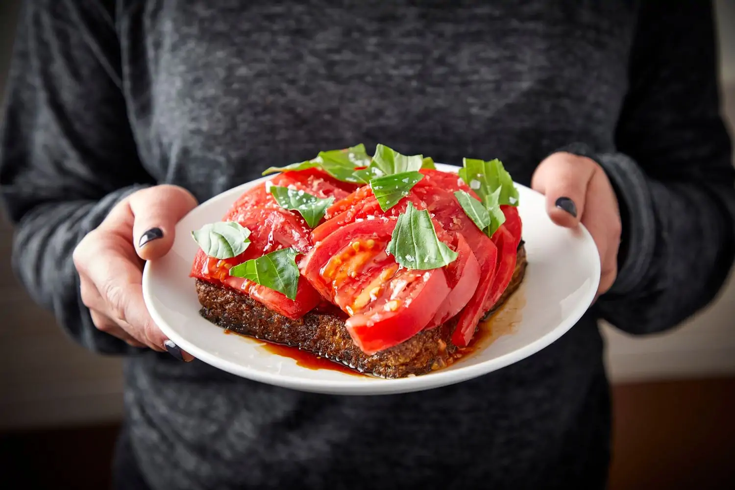 A server holds a white plate with a meatloaf topped with fresh tomatoes, basil leaves and coarse salt at Daisies Chicago. Book on OpenTable.