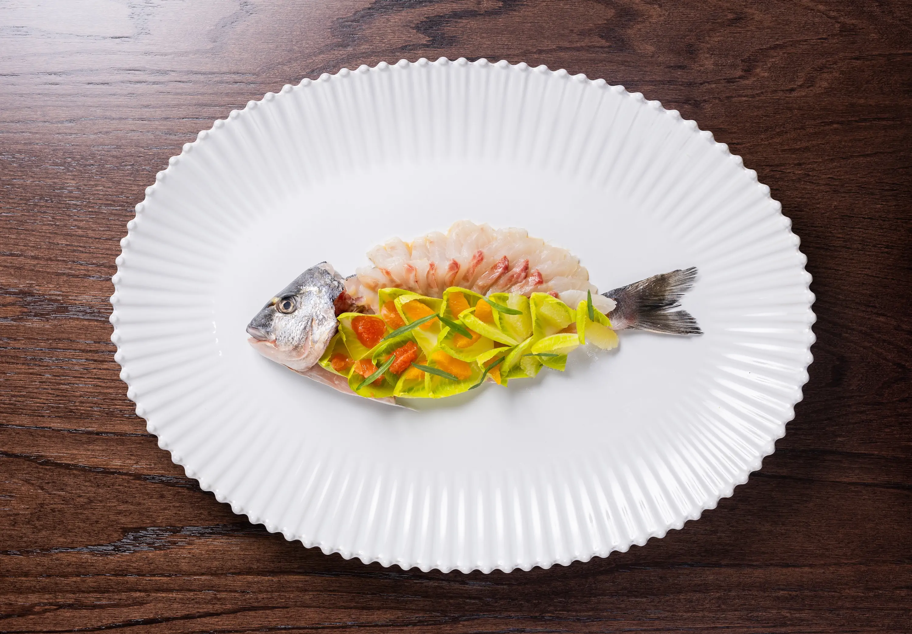 A whole fish fileted and prepared raw with vegetables and fruit on top