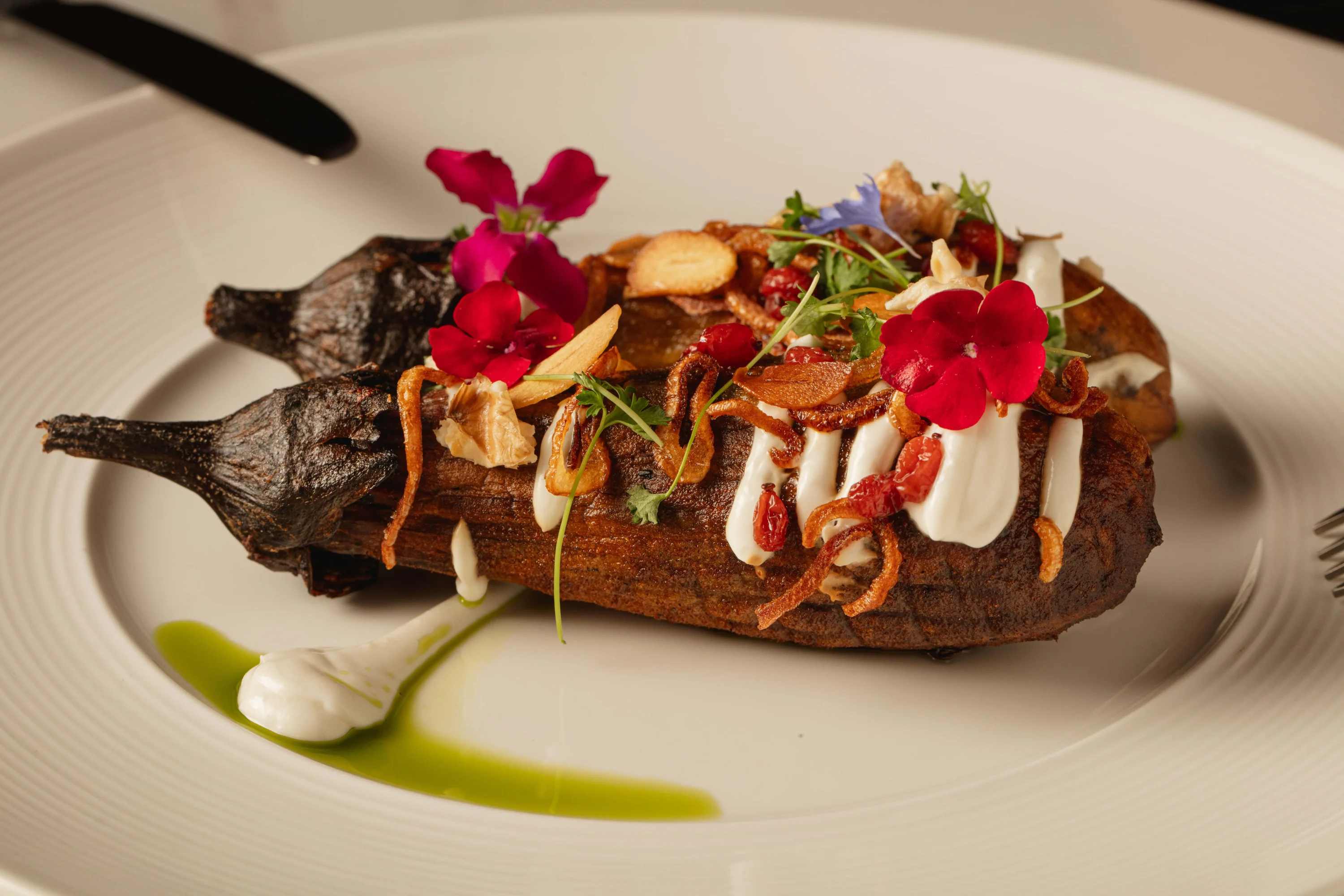 Two grilled eggplants side by side topped with pomegranate seeds, herbs, and yogurt at Perse in Los Angeles