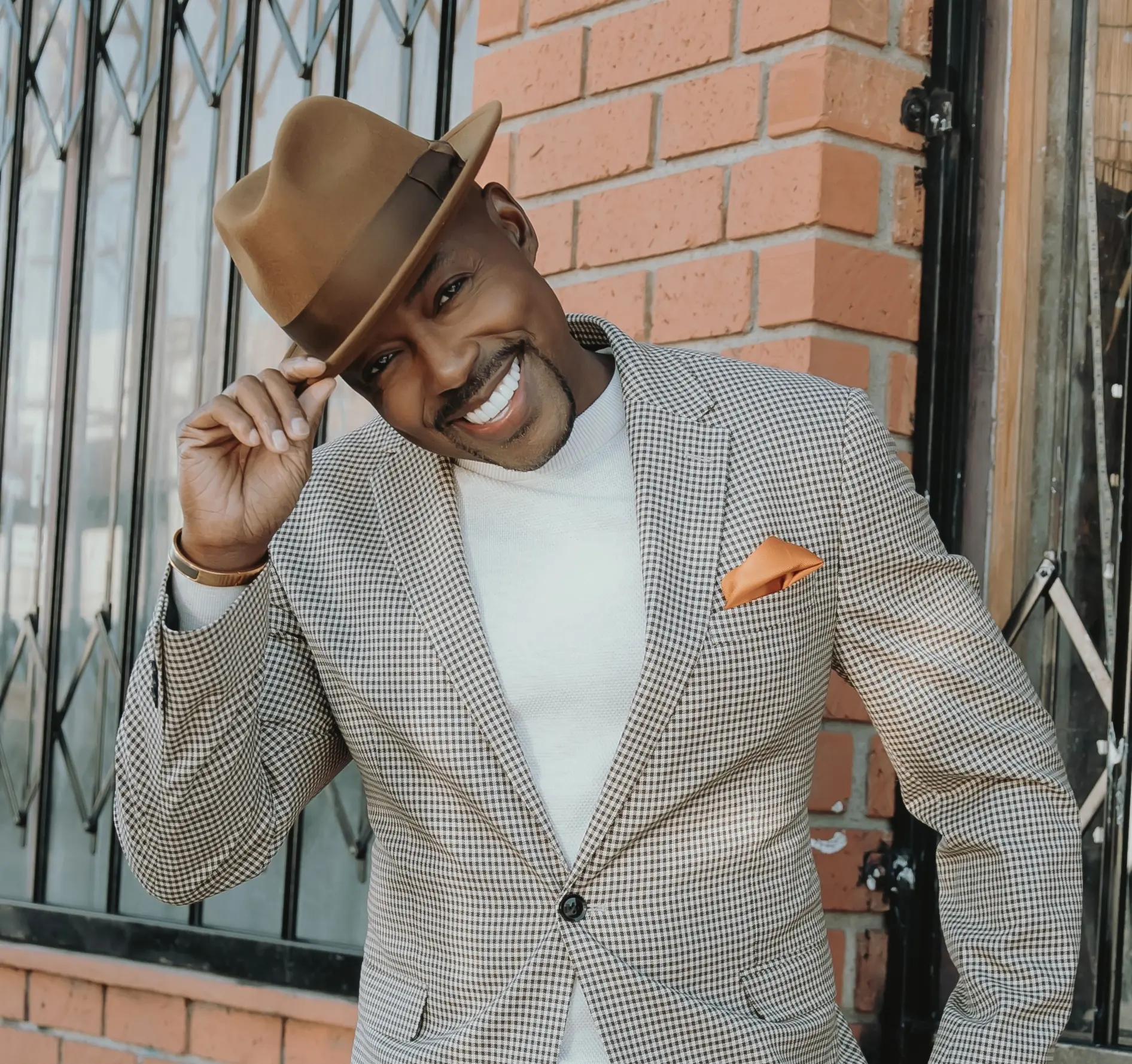 A headshot of the film producer Will Packer wearing a brown hat and a black and white suit