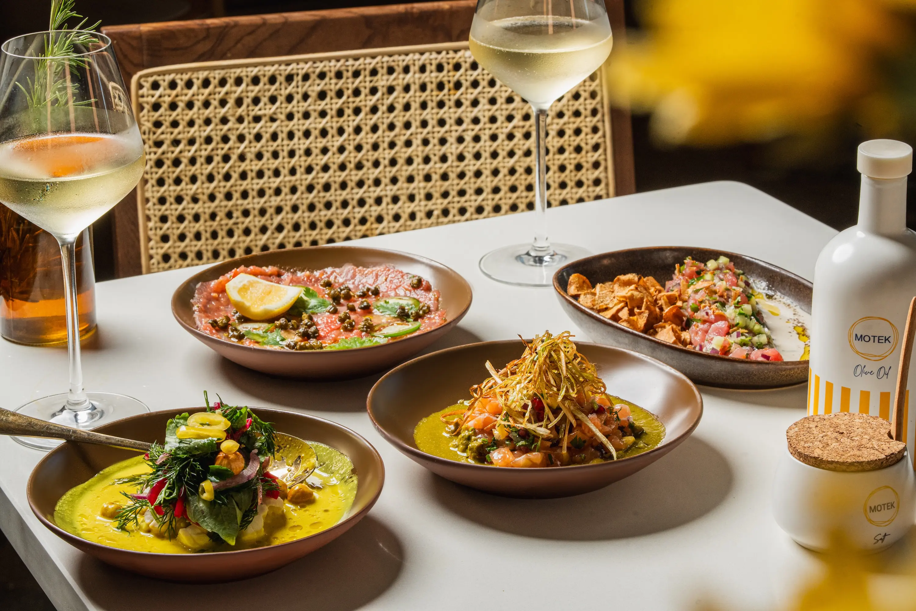 A spread of Mediterranean dishes and some glasses of wine on a wooden table at Motek in the West Village in New York
