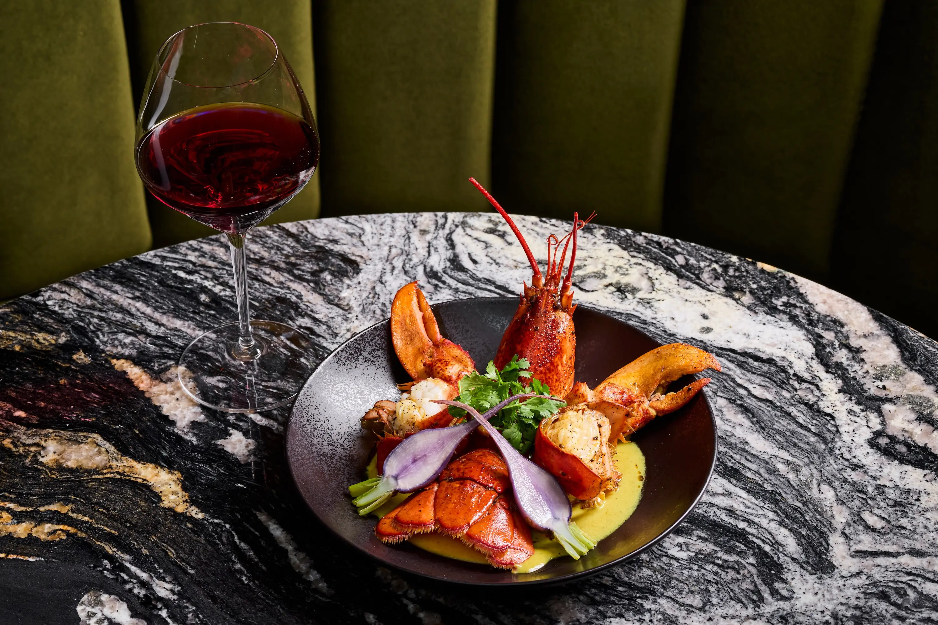 A whole lobster cooked in a yellow sauce next to a glass of red wine at the restaurant AYA in Rohnert Park