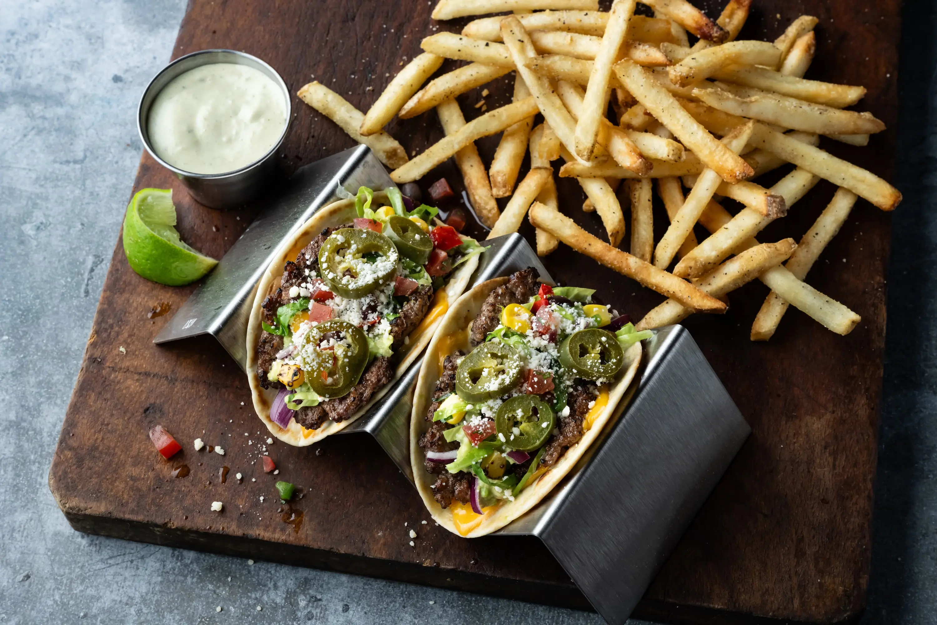 Smashed burger tacos on a taco stand next to ranch dip and French fries at Main Event in Deer Park.