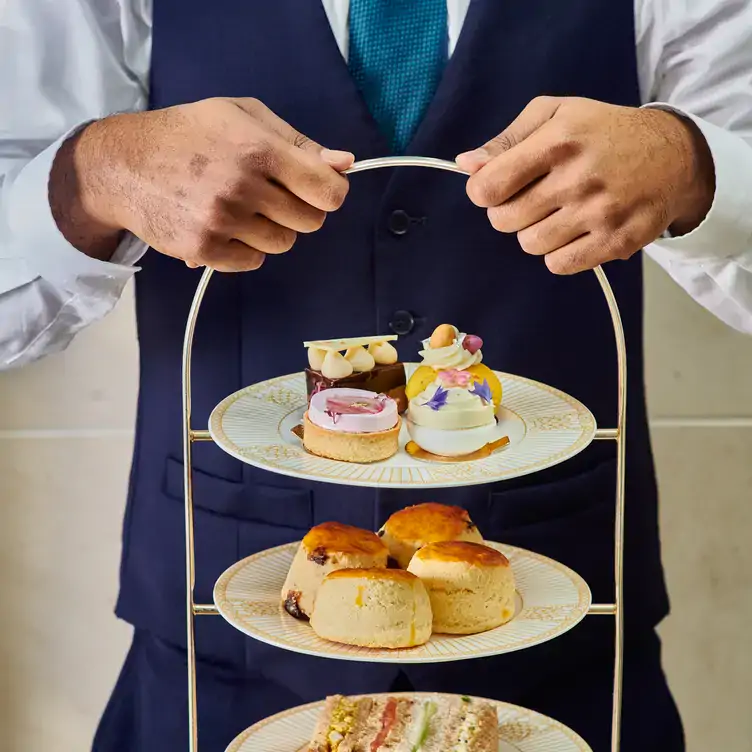 A waiter holding a tiered-tray of pastries and scones at The Landmark Hotel, one of the best Mother's Day afternoon teas in London