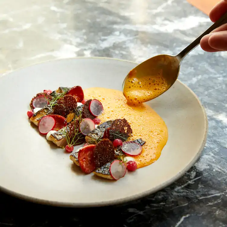 Someone spoons yellow sauce onto a dish at Portland, one of the best affordable MICHELIN restaurants in London.