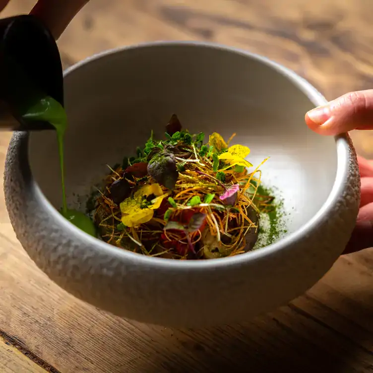 Someone pours green sauce into a bowl with a finely-chopped salad.