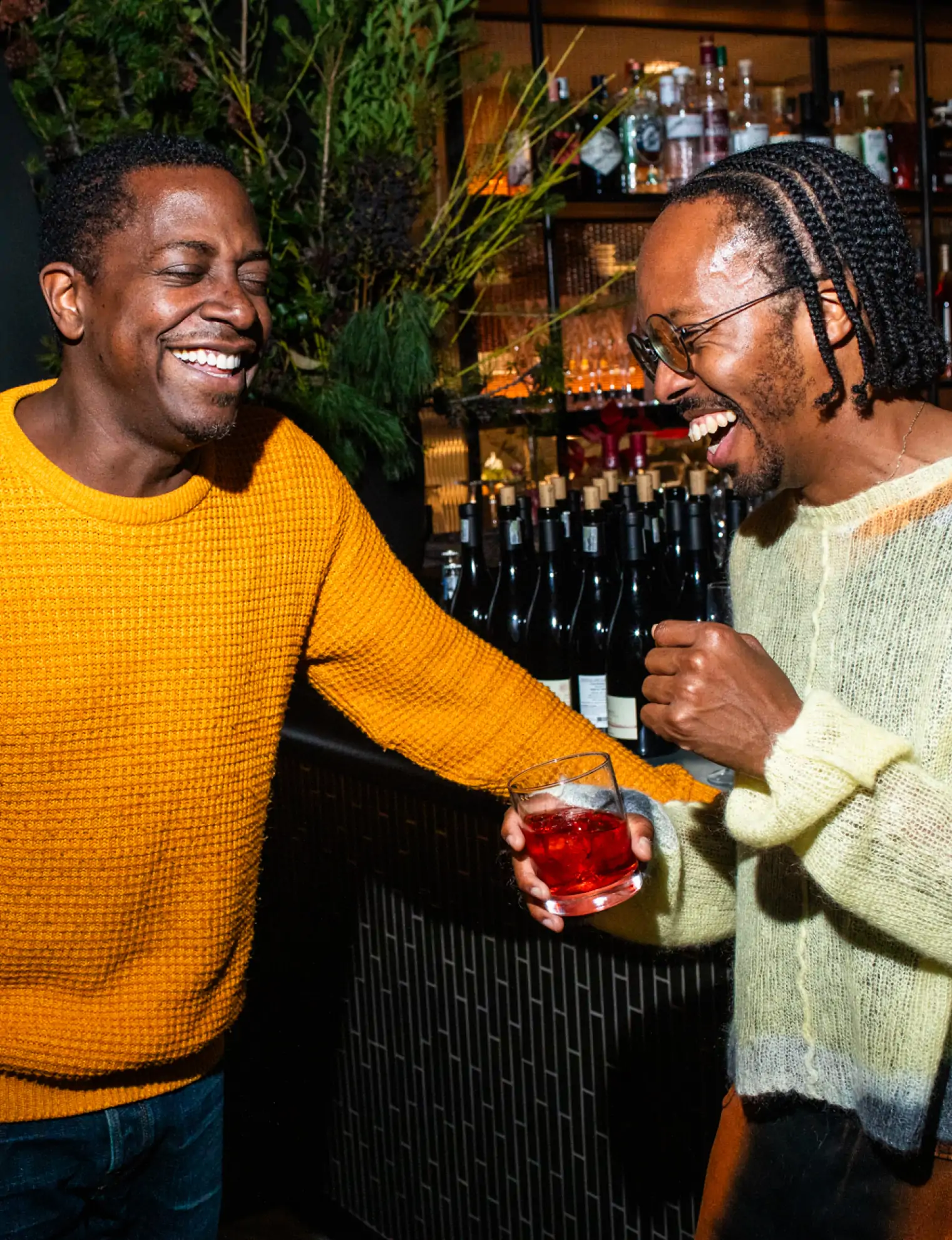 Two men laughing together at a well-stocked bar, one holding a cocktail, illustrating the vibrant social atmosphere of successful events booked through OpenTable Private Dining.
