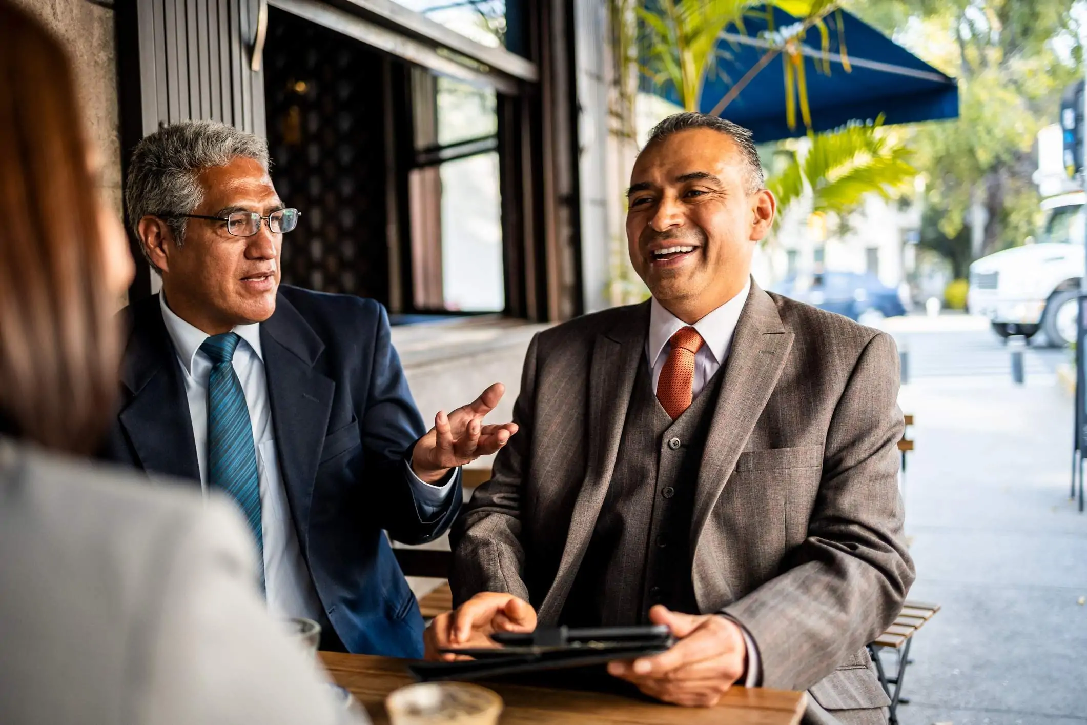 Three business people sit at a restaurant table. They are having a conversation while holding a table to look at data.