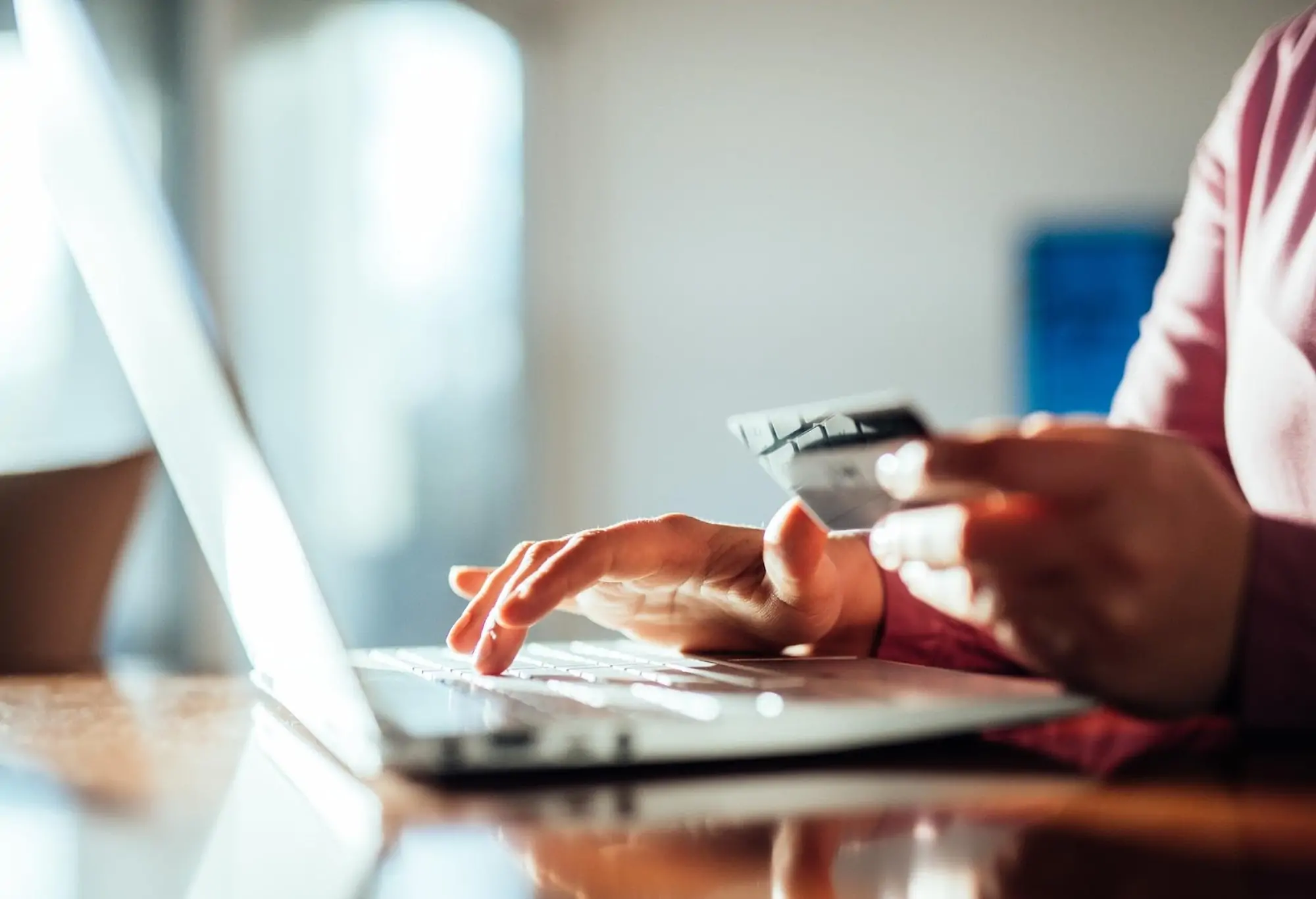 A person holds a credit card while typing on a laptop, making a secure online payment to book a restaurant reservation.