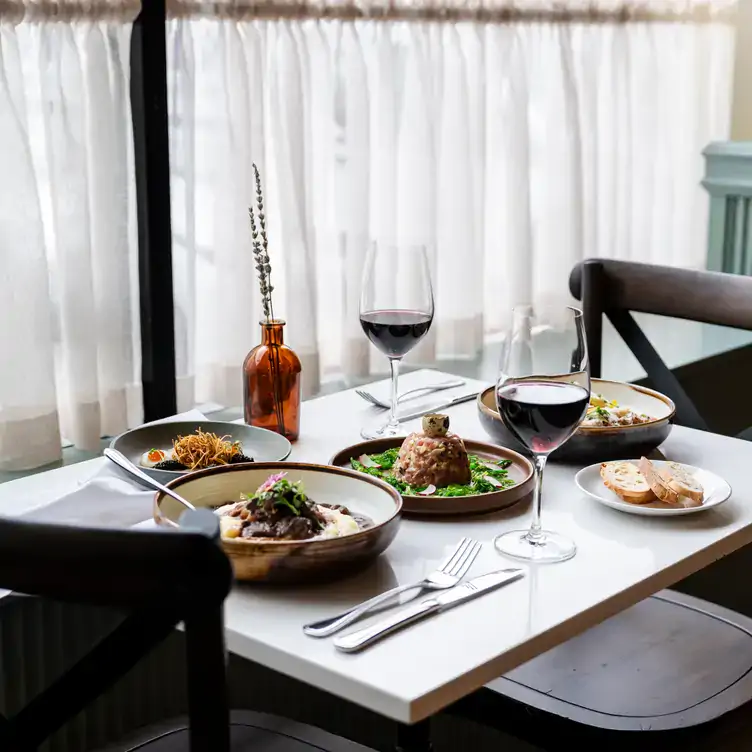 mereon-bistro1 A table by the window laid with dishes and two glasses of red wine at Merèon Bistro, one of the best French restaurants in Vancouver.