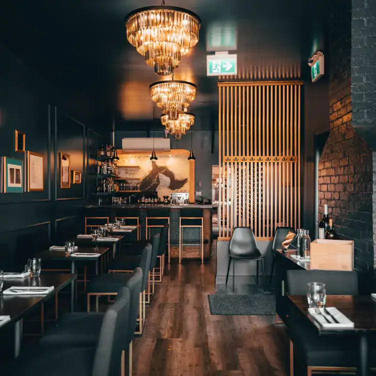 atelier-by-matt-jackson1 The interior of Atelier by Matt Jackson, with chandelier-style lighting, dark furnishing and exposed brick walls.